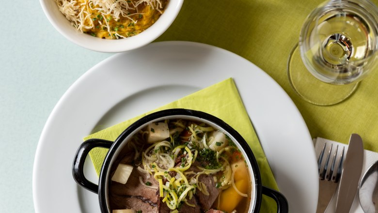 A table with a plate of soup, a bowl of porridge with cheese, a glass of water and cutlery on a green napkin.
