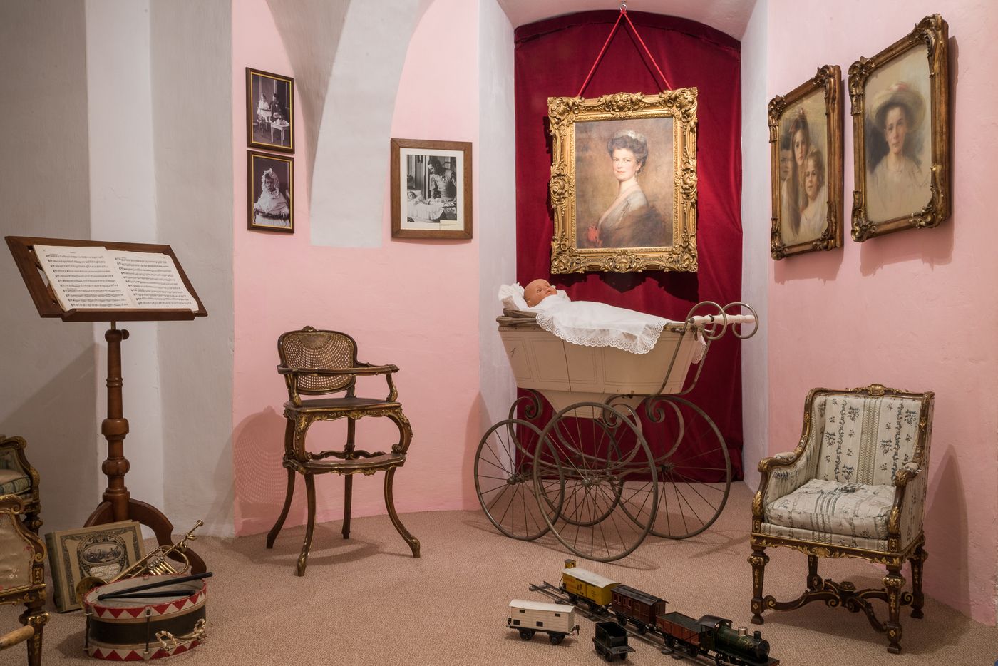 Historic children's room in the museum with antique baby carriage, chairs and toy train.