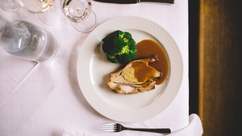 Stuffed veal breast with broccoli and sauce on a white plate.