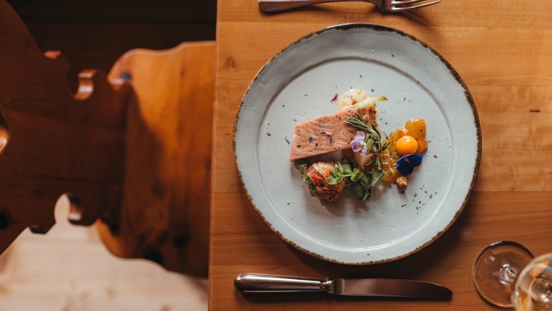 A plate of smoked catfish fillet and celery and peanut salad, decorated with edible flowers, on a wooden table.