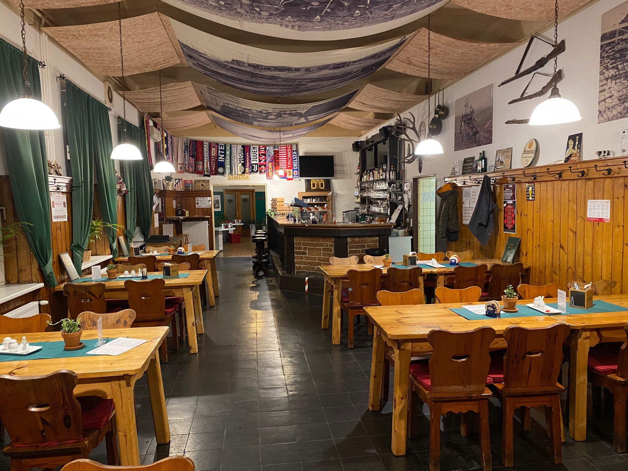 Cozy dining room with wooden tables, chairs and bar, decorated with soccer scarves and rustic elements.