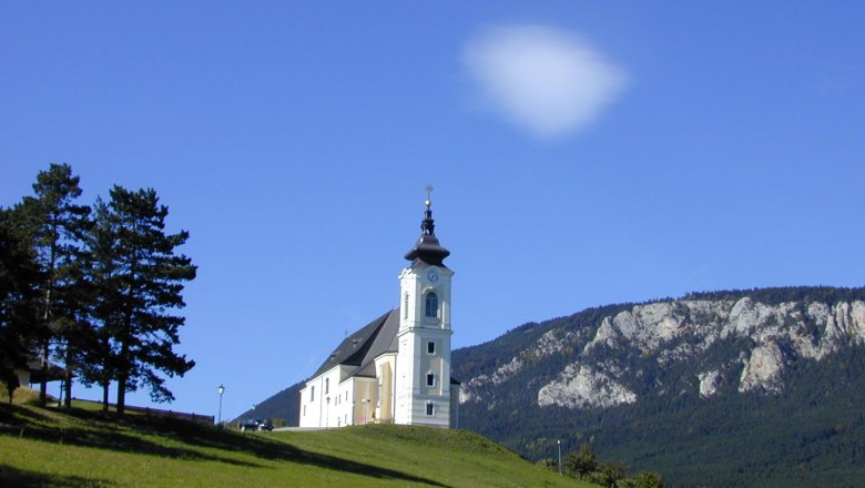 Church on a hill with blue sky and mountains in the background.