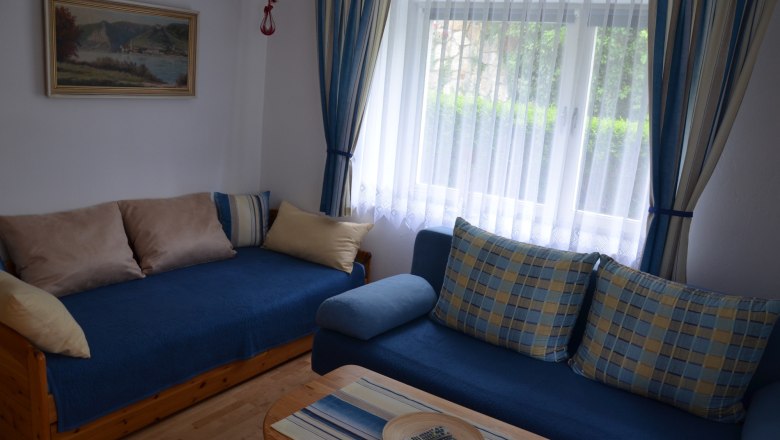 Cozy living room with blue sofas, cushions, a wooden table and a window with curtains.