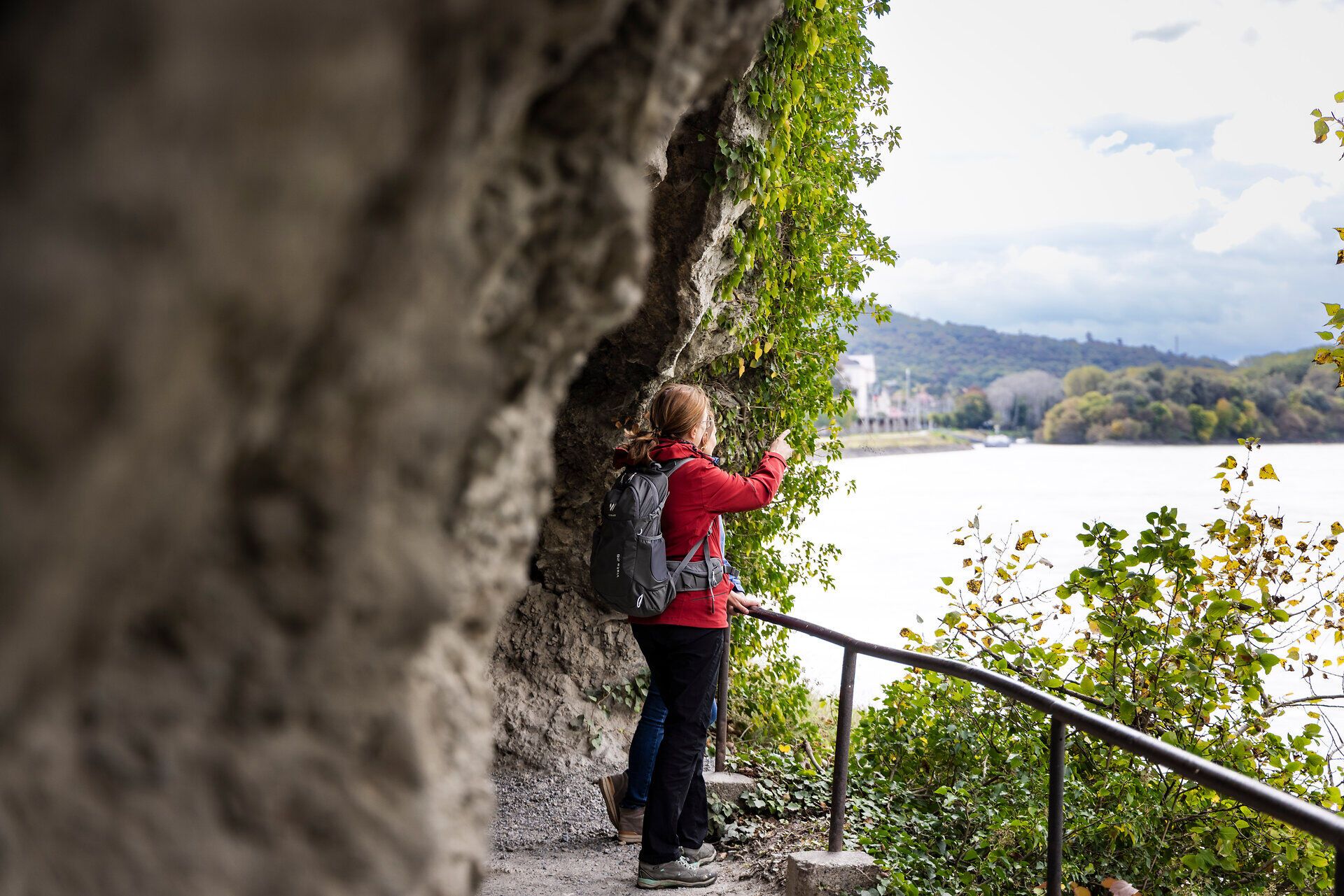 Two women on a hiking trail look out over the water. Rocks in the background. 