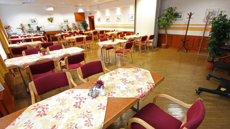 An empty dining room with laid tables and red chairs.