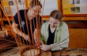 Two women work together on a basket weaving project in a workshop.