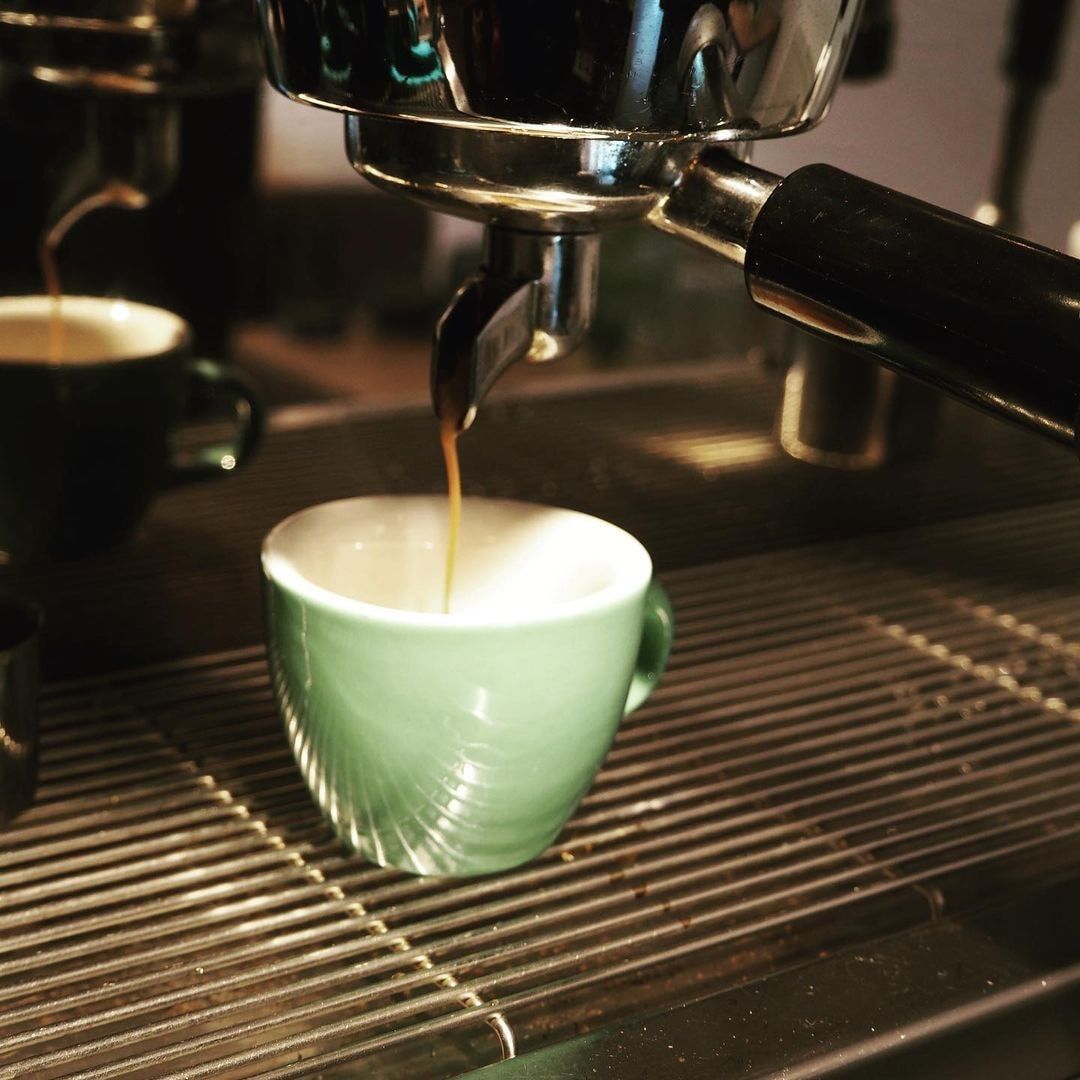 Espresso machine fills a green cup with coffee.