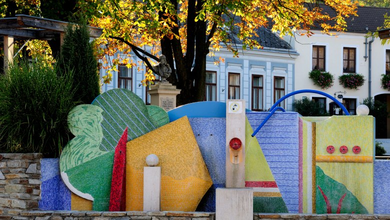 Colorful fountain in Maissau with mosaic decorations and autumn trees in the background.