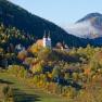 Autumn landscape with church in Maria Schutz, surrounded by colorful trees and hills.