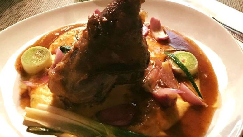 A plate with a meat dish, served on mashed potatoes with a brown sauce and vegetables.