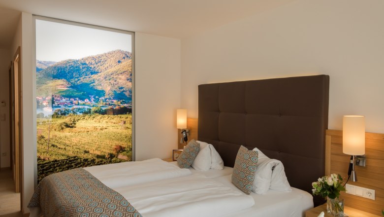 Modern hotel room with double bed, decorative cushions and large landscape picture on the wall.