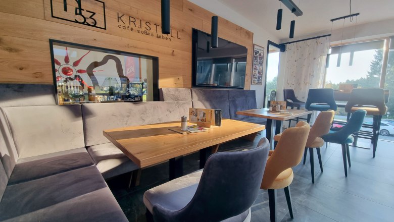 Interior view of a modern café with wooden walls, comfortable chairs and large windows that let in sunlight.