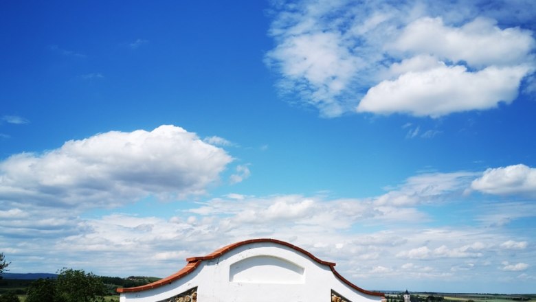 Small stone house in a vineyard under a blue sky with clouds.