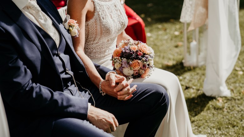 A bridal couple sits outside, the bride holds a bouquet of flowers.