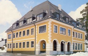 Yellow building with a gray roof and many windows, surrounded by snow.