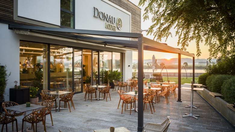 Terrace of the Donau Lodge Ybbs at sunset with tables and chairs.