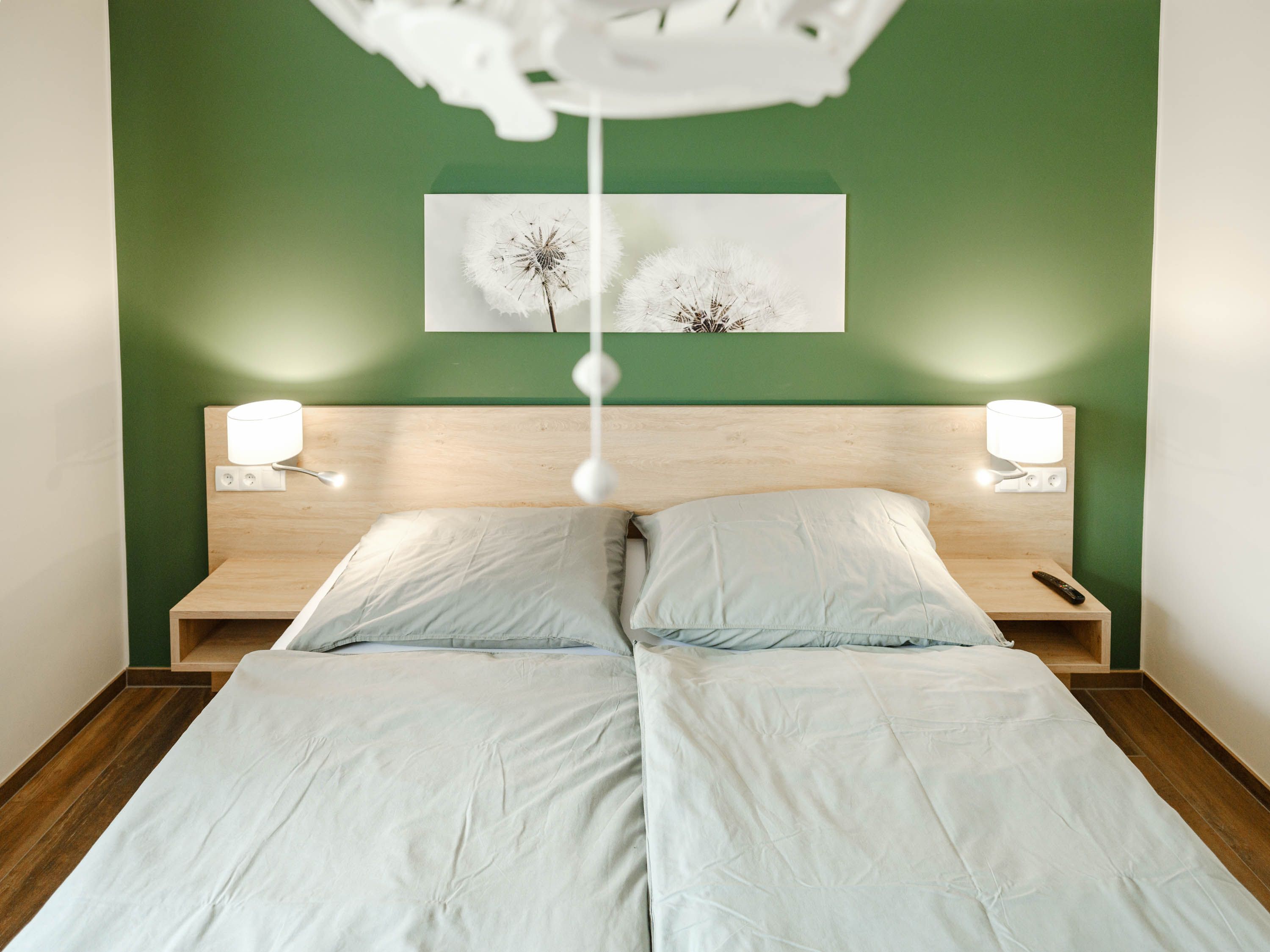 Modern bedroom with green-painted wall, double bed and two bedside lamps.