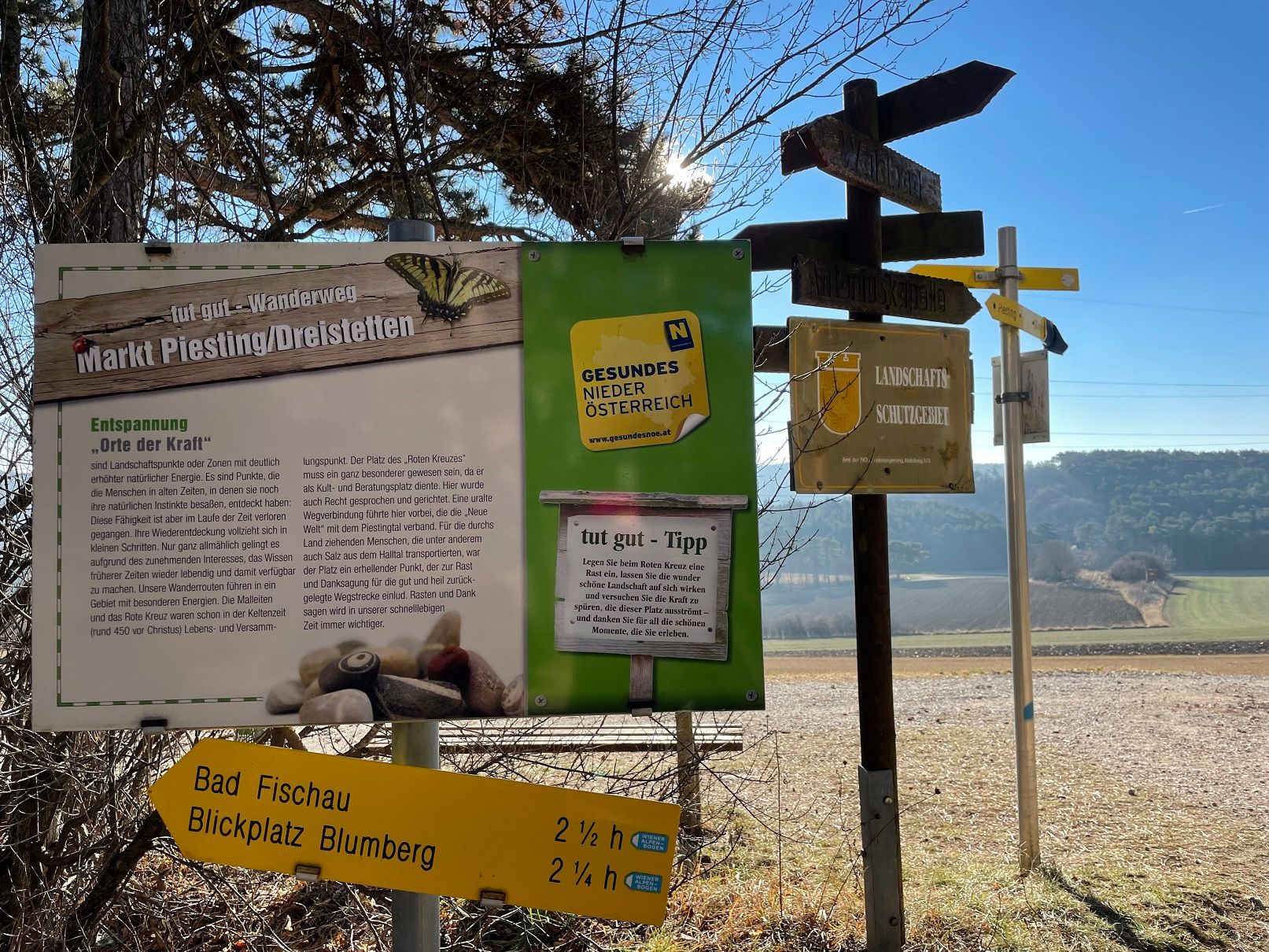 Signpost and information board in a rural landscape with a blue sky.