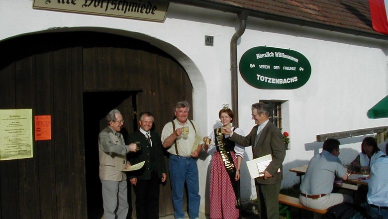 Group of people clinking glasses in front of the old village smithy in Totzenbach.