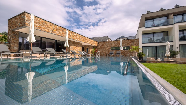Exterior view of a modern hotel with pool and sun loungers.