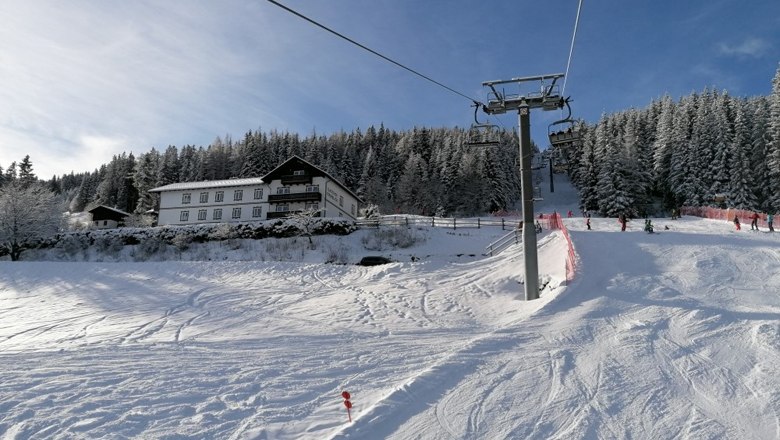 Snow-covered ski slope with ski lift and forest in the background.