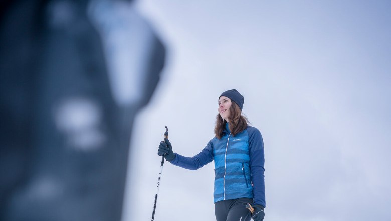 A woman cross-country skiing on a snow-covered surface with houses in the background.