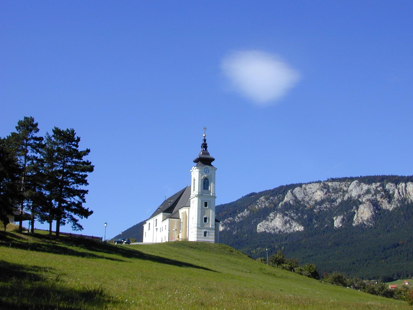 Church on a hill with blue sky and mountains in the background.