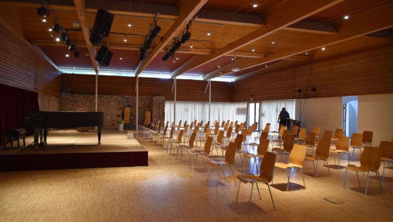 An empty event hall with chairs and a grand piano on the stage.