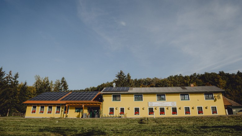 Yellow building with solar panels on the roof, surrounded by trees.