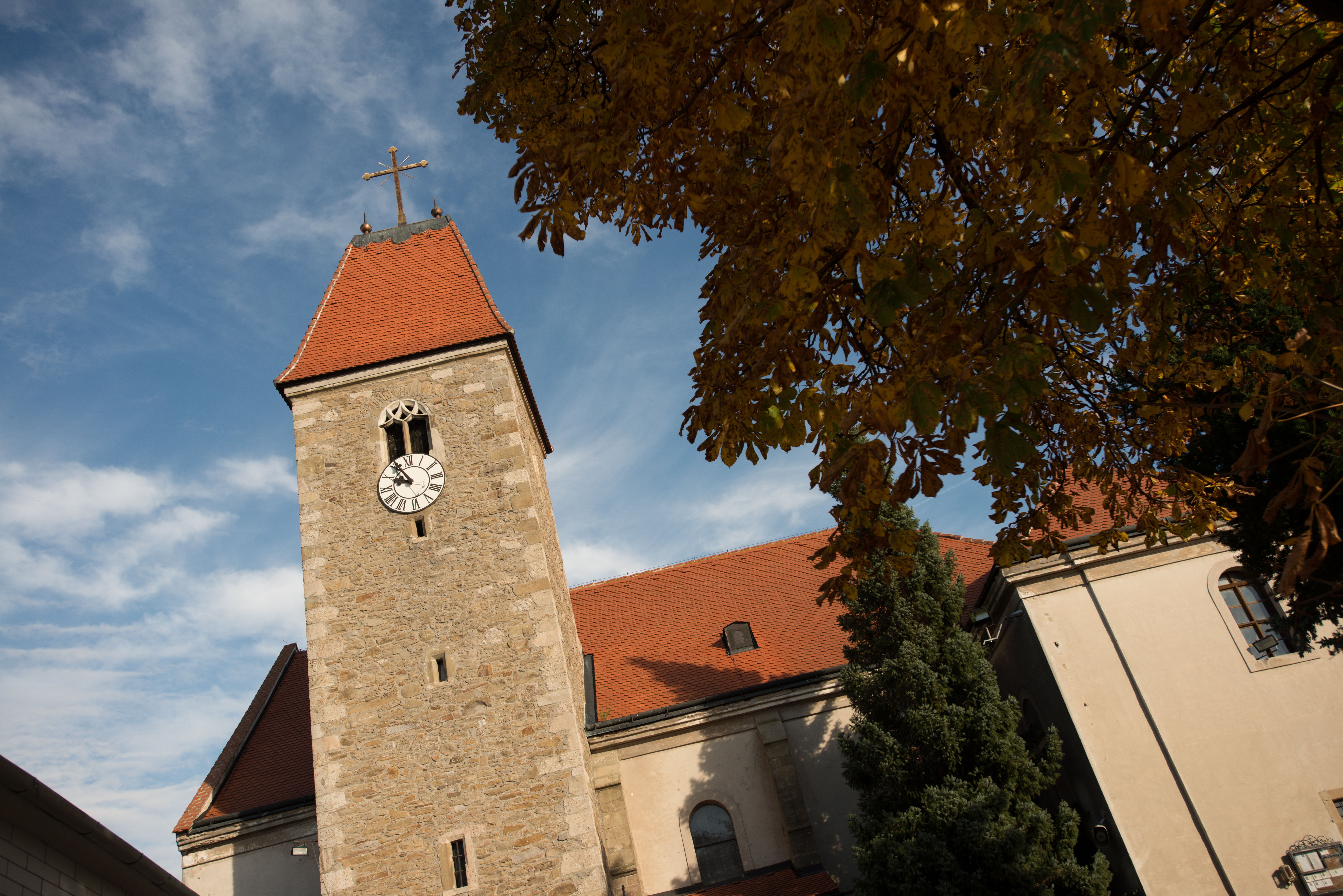 Weissenkirchen church tower with clock and red roof, surrounded by autumn leaves and blue sky.