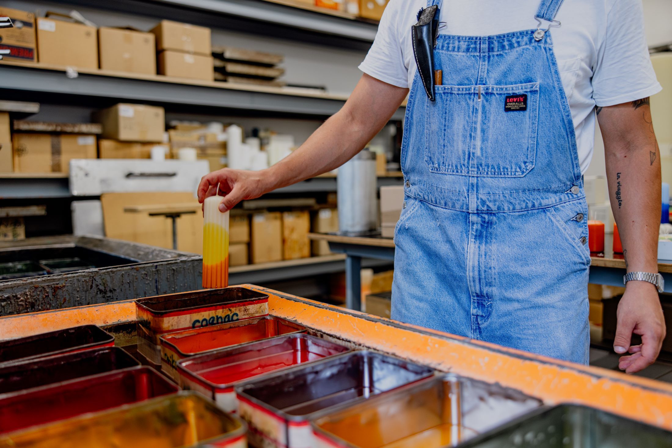 Person in dungarees dips candle in paint bath.