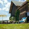A farmhouse with a wooden façade, garden furniture and parasol on a meadow in sunny weather.