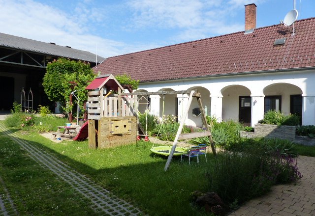 An inner courtyard with a playground, surrounded by a building with red roof tiles and white walls.