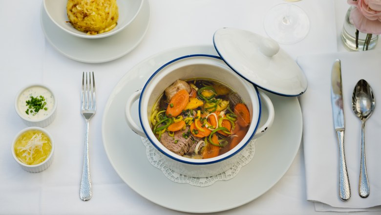 A table set with a stew in a white pot, a dumpling, two sauces and a glass of white wine.