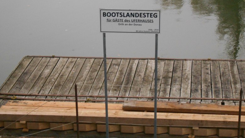 Wooden jetty with sign 'Boat landing stage for guests of the Uferhaus' on a quiet stretch of water.