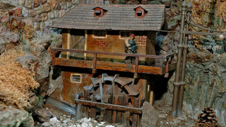 Miniature water mill with wooden wheel and small building in rocky surroundings.