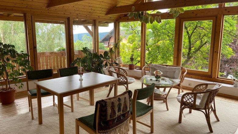 A bright room with wooden furniture, large windows and plants.