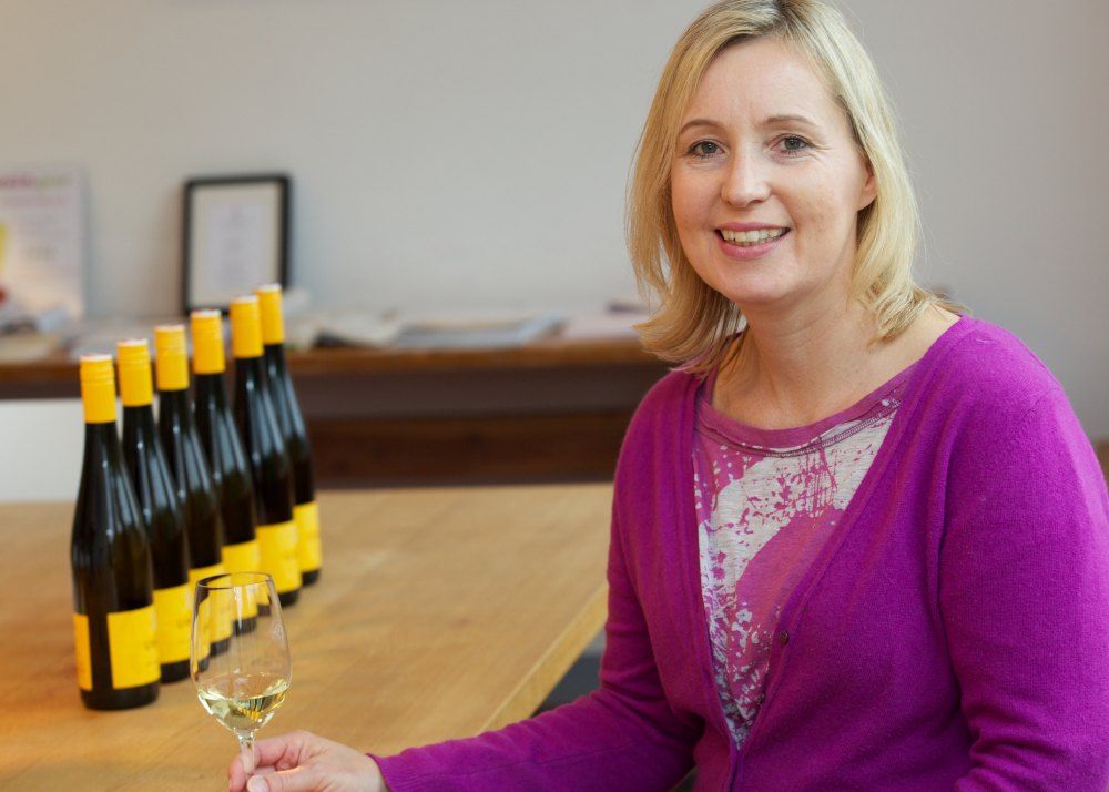 Woman in purple sweater with wine glass, bottles in the background.