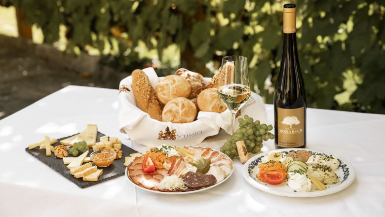 Heurigen snack with bread, cheese, cold cuts, wine and grapes on a table.