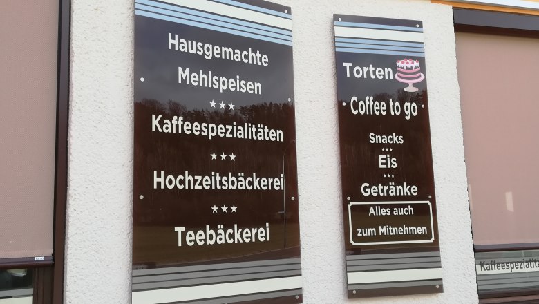 Two brown signs on the wall with coffee house offers such as pastries and ice cream.