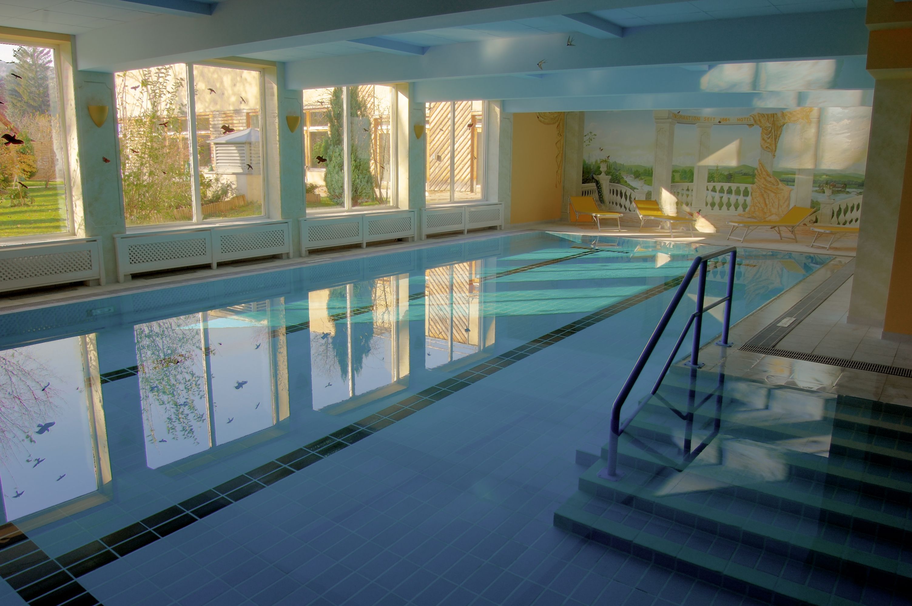 Indoor pool at Hotel Marienhof with large windows and sun loungers.