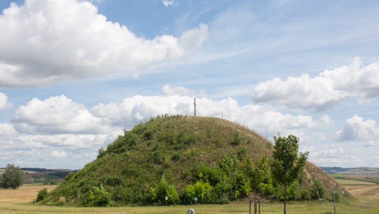 A grassy hill with a cross on top under a cloudy sky.