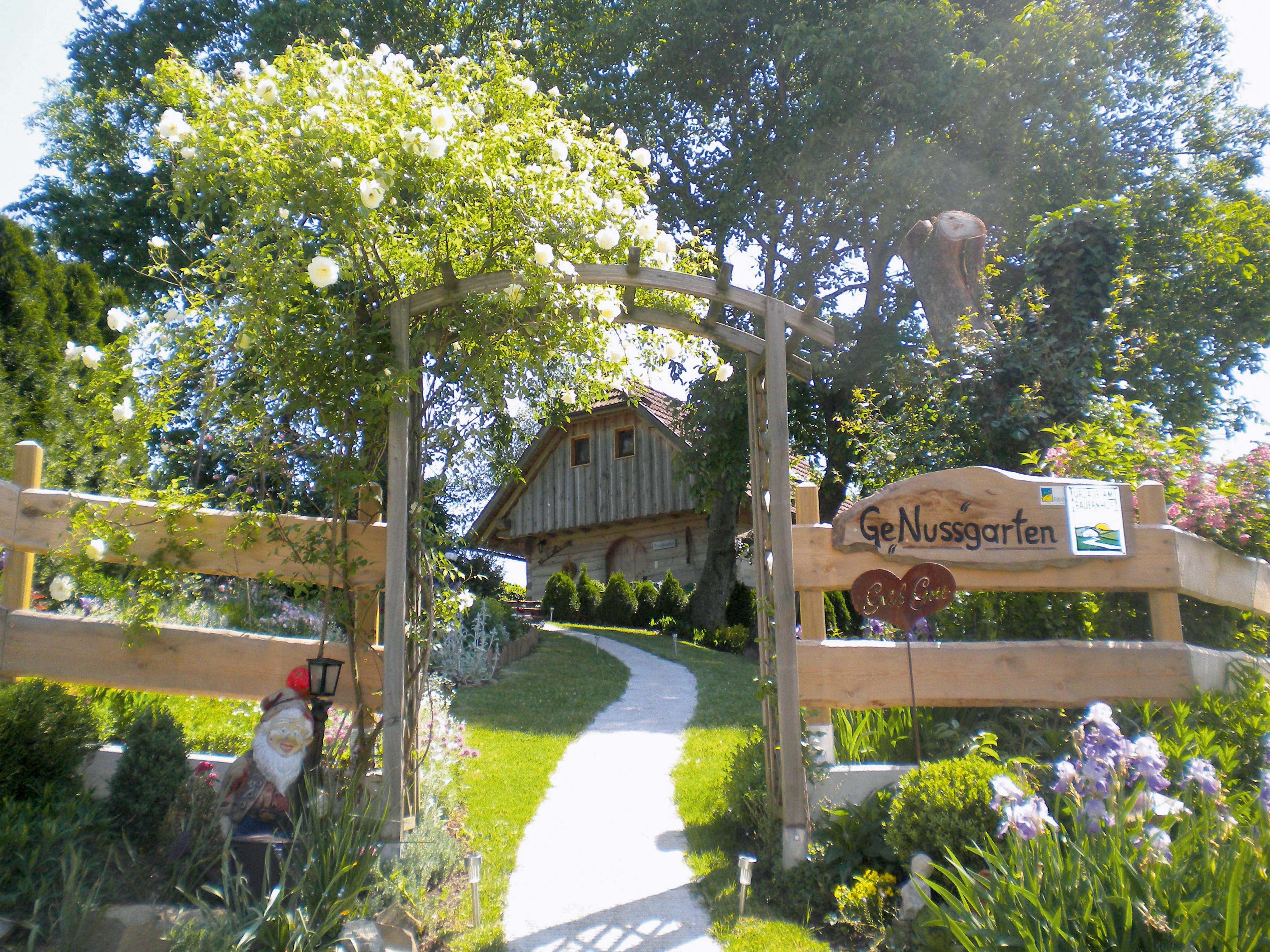 Entrance to a garden with wooden gate and 'GeNussgarten' sign.