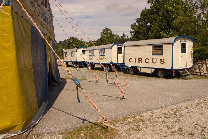 Circus wagon and tent on a gravel site.