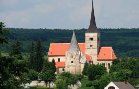 St. Michael's Church in Pulkau with a red roof and pointed tower, surrounded by trees.