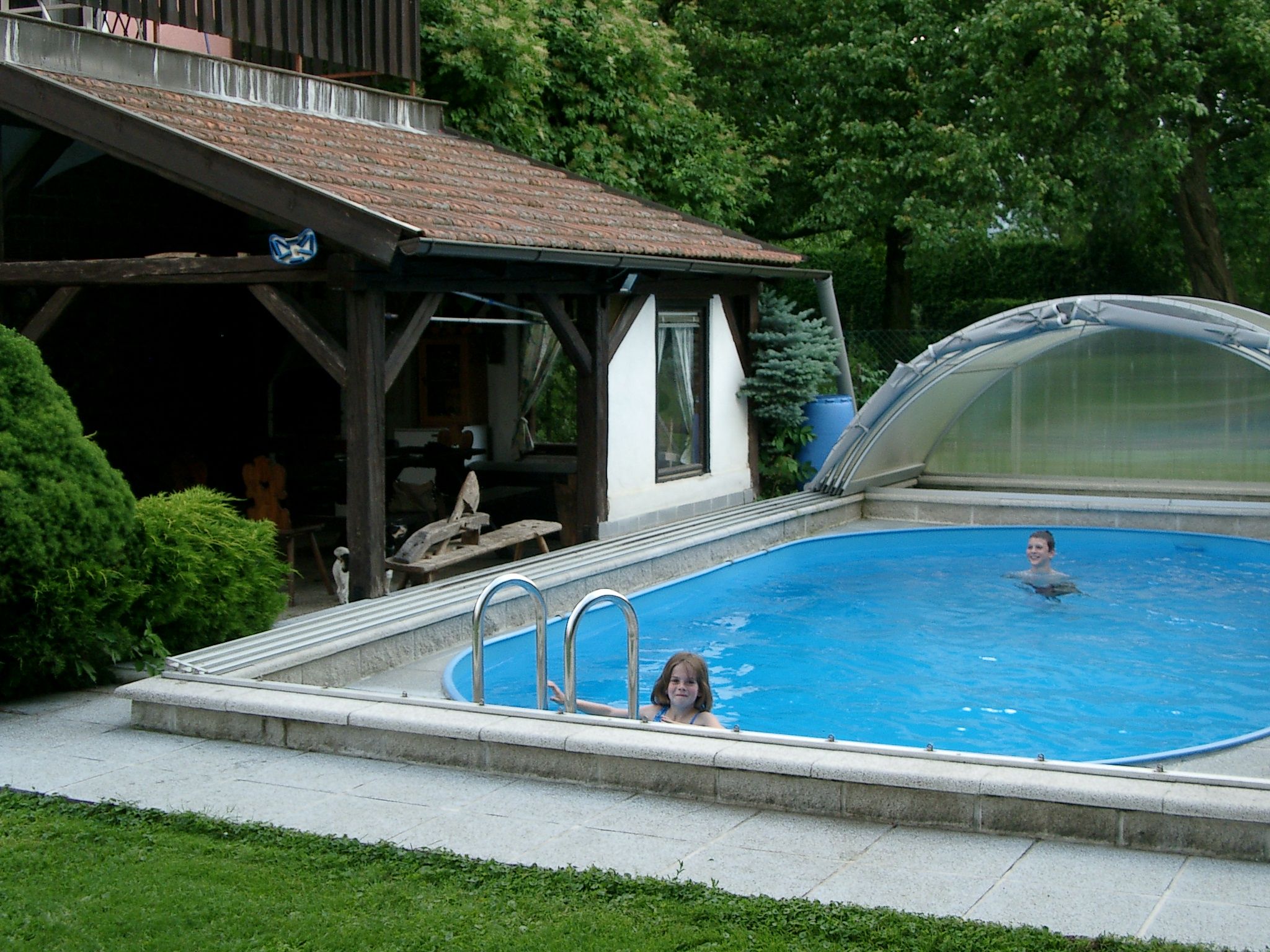 Two children swim in a small, covered pool next to a wooden pavilion.