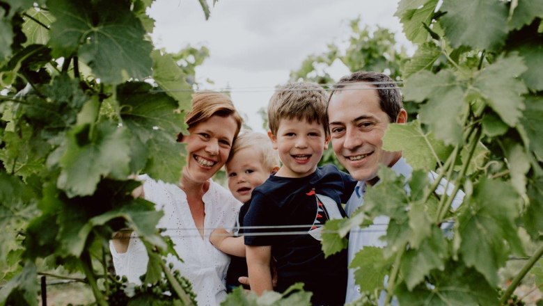 A smiling family stands among grapevines in a vineyard.