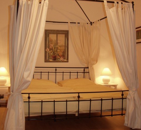 Canopy bed, © Hotel Residenz Schrannenhof A four-poster bed with white curtains in a cozy bedroom, illuminated by two bedside lamps.