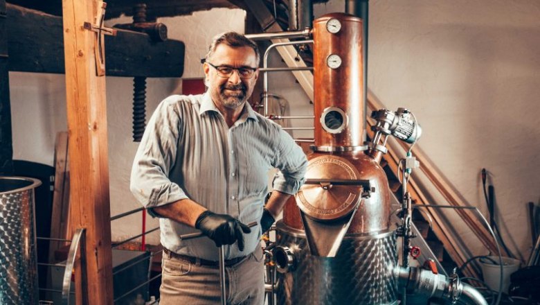 A man stands next to a copper still in a distillery.