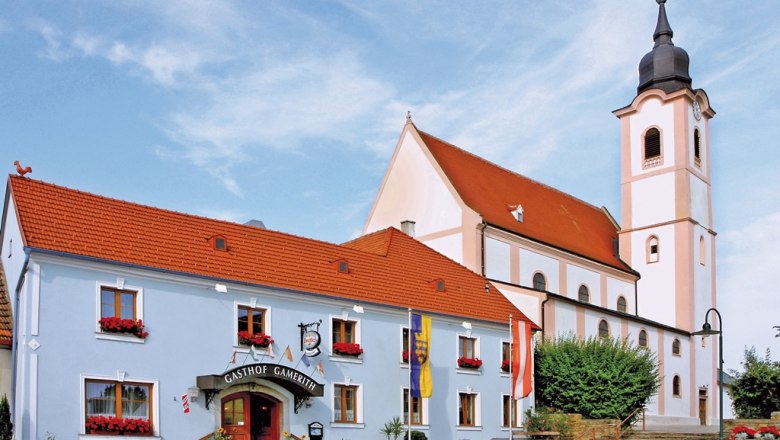 Gasthaus Gamerith next to a church with a tower and red roof.